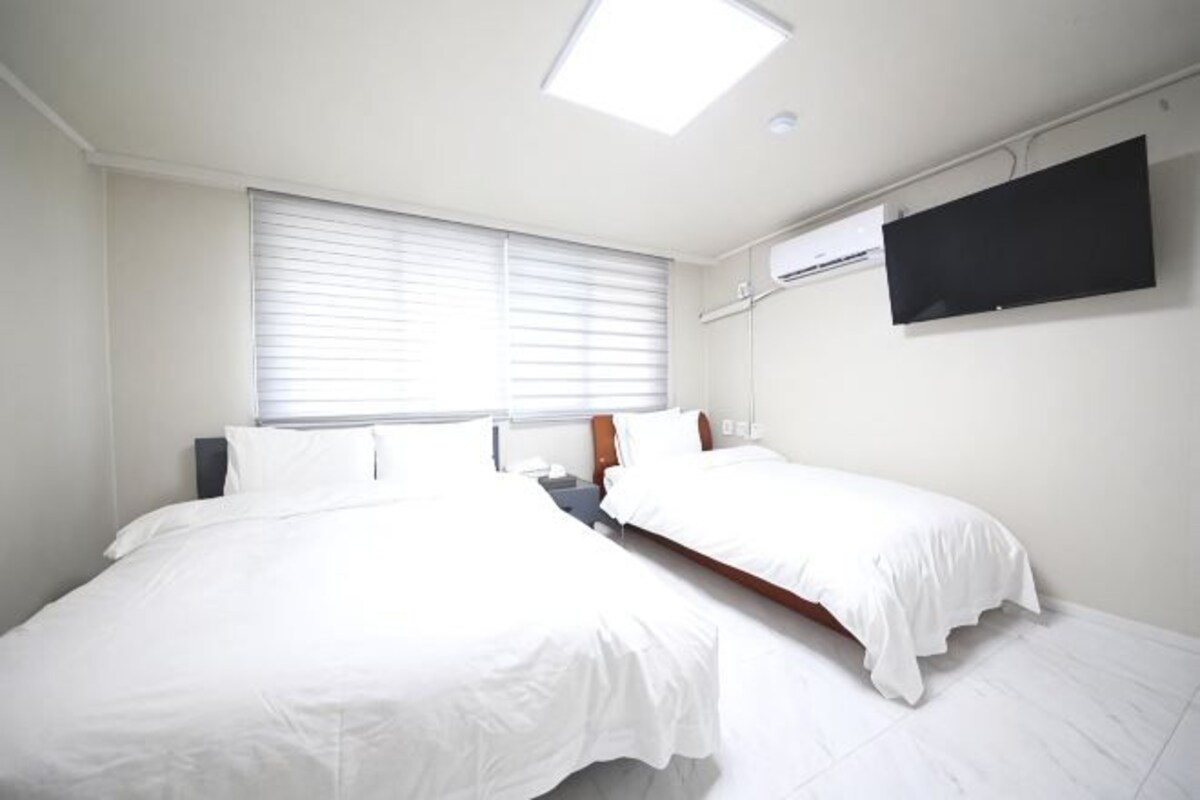 Habitación de hotel con dos camas, un televisor de pantalla plana y una ventana con persianas.