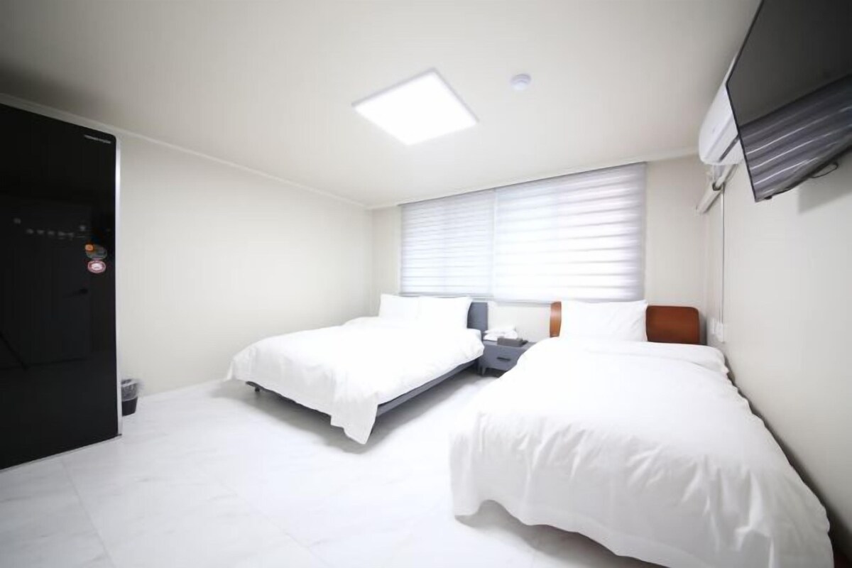 A hotel room with two beds, a desk, a chair, a TV, and a window with blinds.