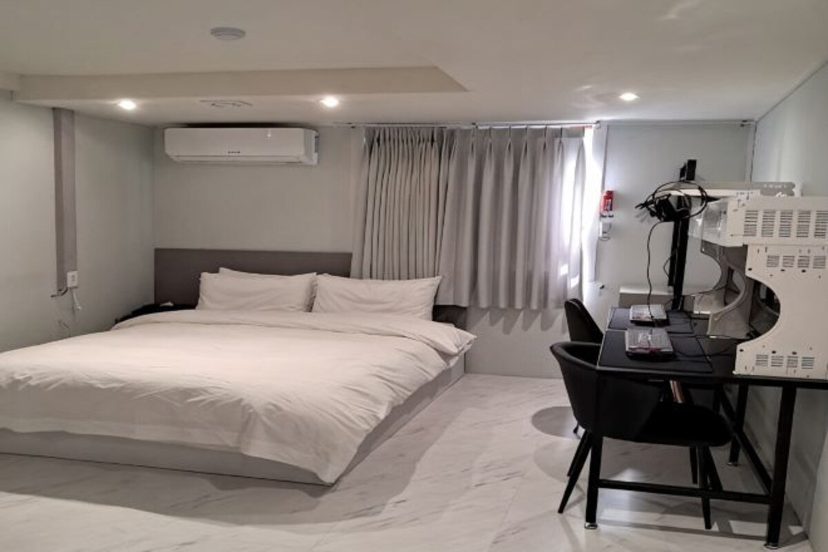 Habitación de hotel con cama, escritorio con ordenador, aire acondicionado y ventana con cortinas.