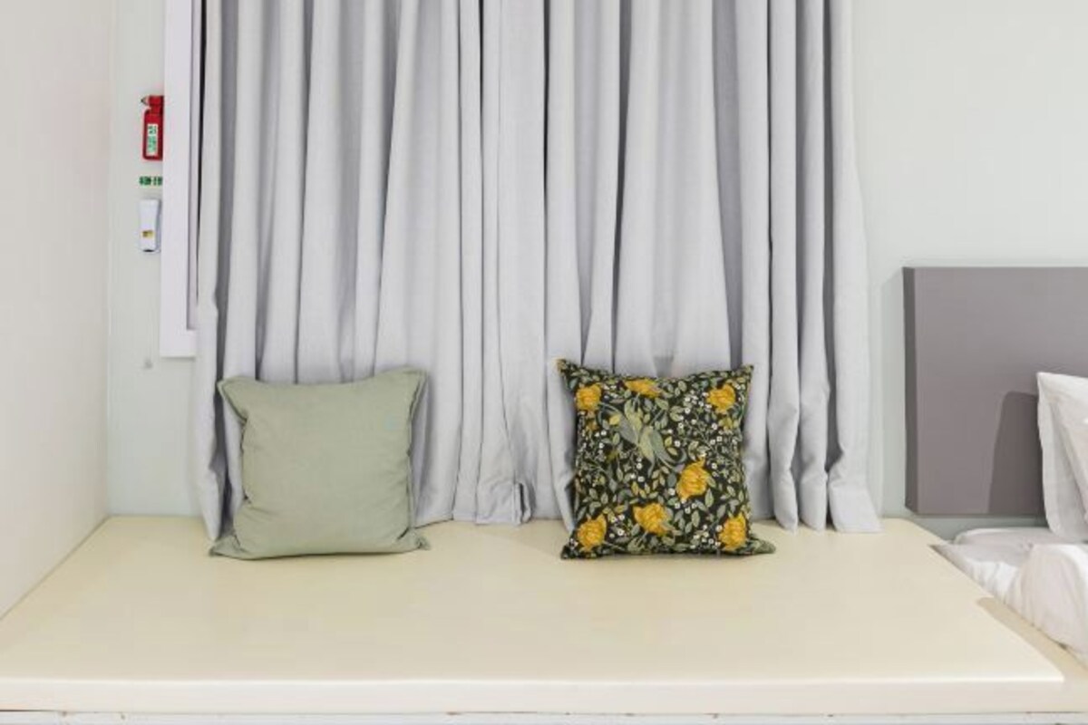 Una cama con cabecera blanca, cortina gris y almohada verde.