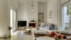 A modern living room with a fireplace, a dining area with a table set for two, and a TV in the background. - Adhilli i residence (Rethymno)