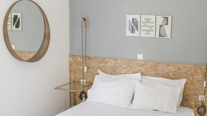 A neatly made bed with white linens and two rolled towels, a wooden headboard, a chandelier, a round mirror, and framed artwork on the wall. - Adhilli i residence (Rethymno)