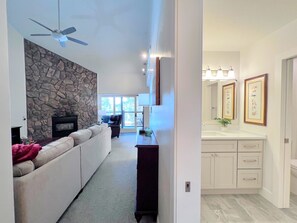 A modern living room with a stone wall, a fireplace, a ceiling fan, and a view to the outside. - Park Place Aspen Condo • Walk to Main St. • Snowflake Lift • Pool+Hot Tubs (Breckenridge)