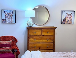 A bedroom with a wooden dresser, a mirror, two framed animal paintings, a red chair, and a bed with a white blanket. - Park Place Aspen Condo • Walk to Main St. • Snowflake Lift • Pool+Hot Tubs (Breckenridge)