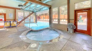A hot tub area with a wooden ceiling, large windows, and a view of the outdoor pool area.