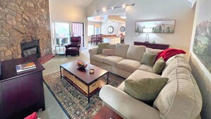 A spacious living room with a stone wall, a fireplace, a large sofa, a coffee table, and a ceiling fan.