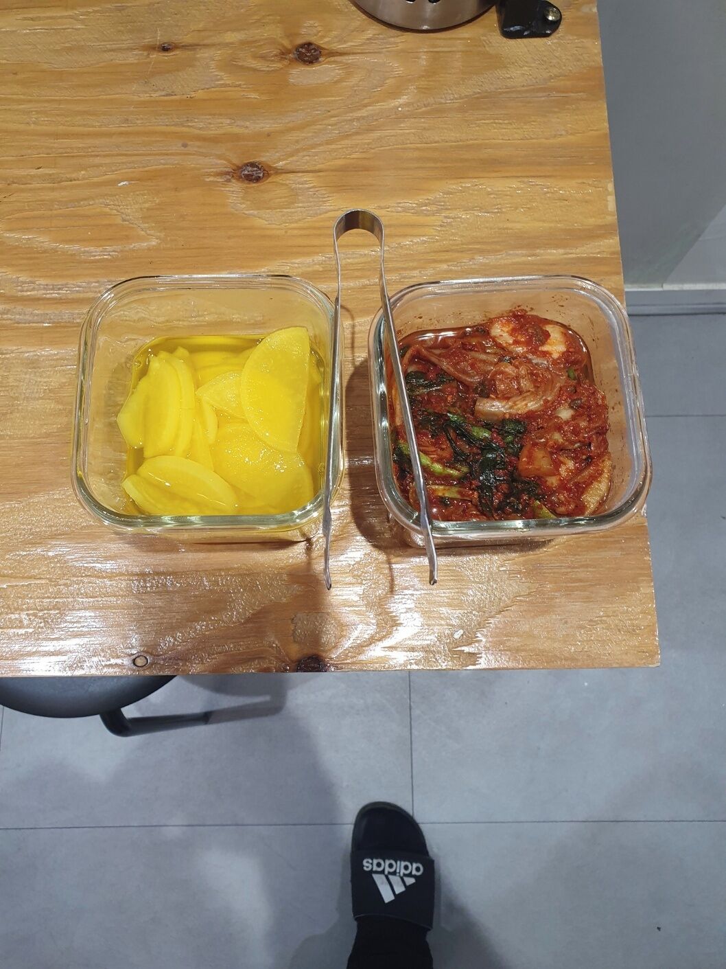 Two glass dishes on a wooden table, one with yellow slices and the other with a red sauce and vegetables.