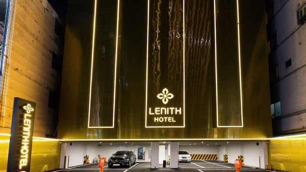 The exterior of the Lenith Hotel with illuminated vertical panels and a parking area with marked spaces. - Lenith Hotel Seomyeon (Busan)