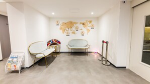 A waiting area with a world map on the wall, a white bench, a white chair, and a magazine rack. - Lenith Hotel Seomyeon (Busan)