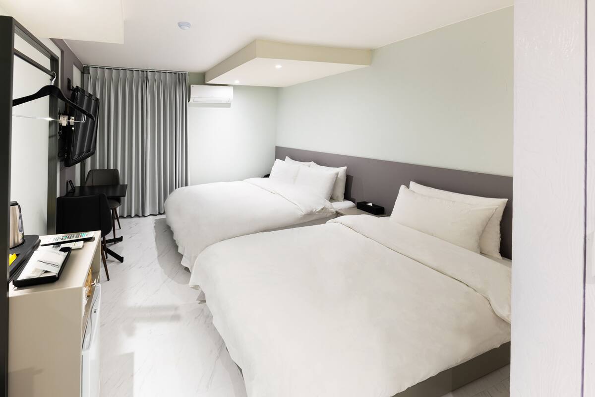 Une chambre d’hôtel avec deux lits, un bureau avec une chaise, une télévision et une fenêtre avec des rideaux.