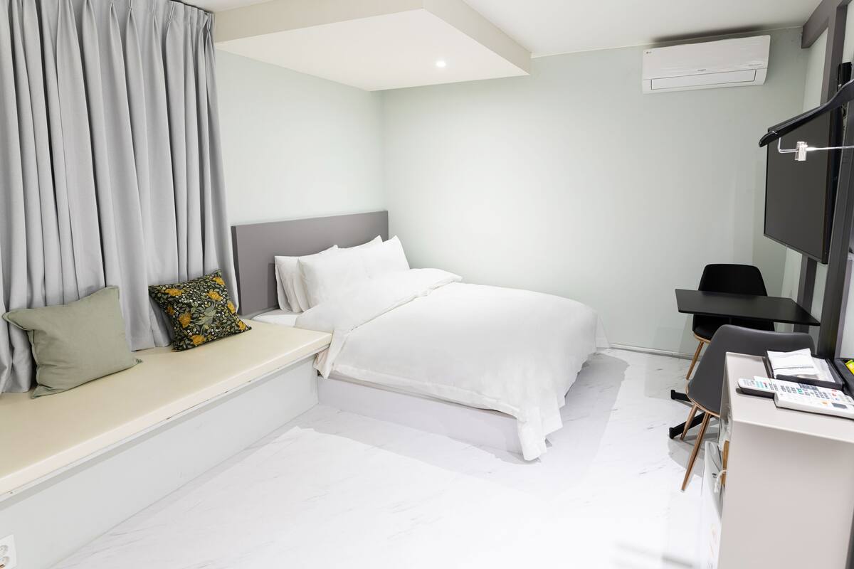 Une chambre d’hôtel moderne équipée d’un lit, d’un bureau, d’une chaise, d’une télévision et d’une fenêtre avec des rideaux.