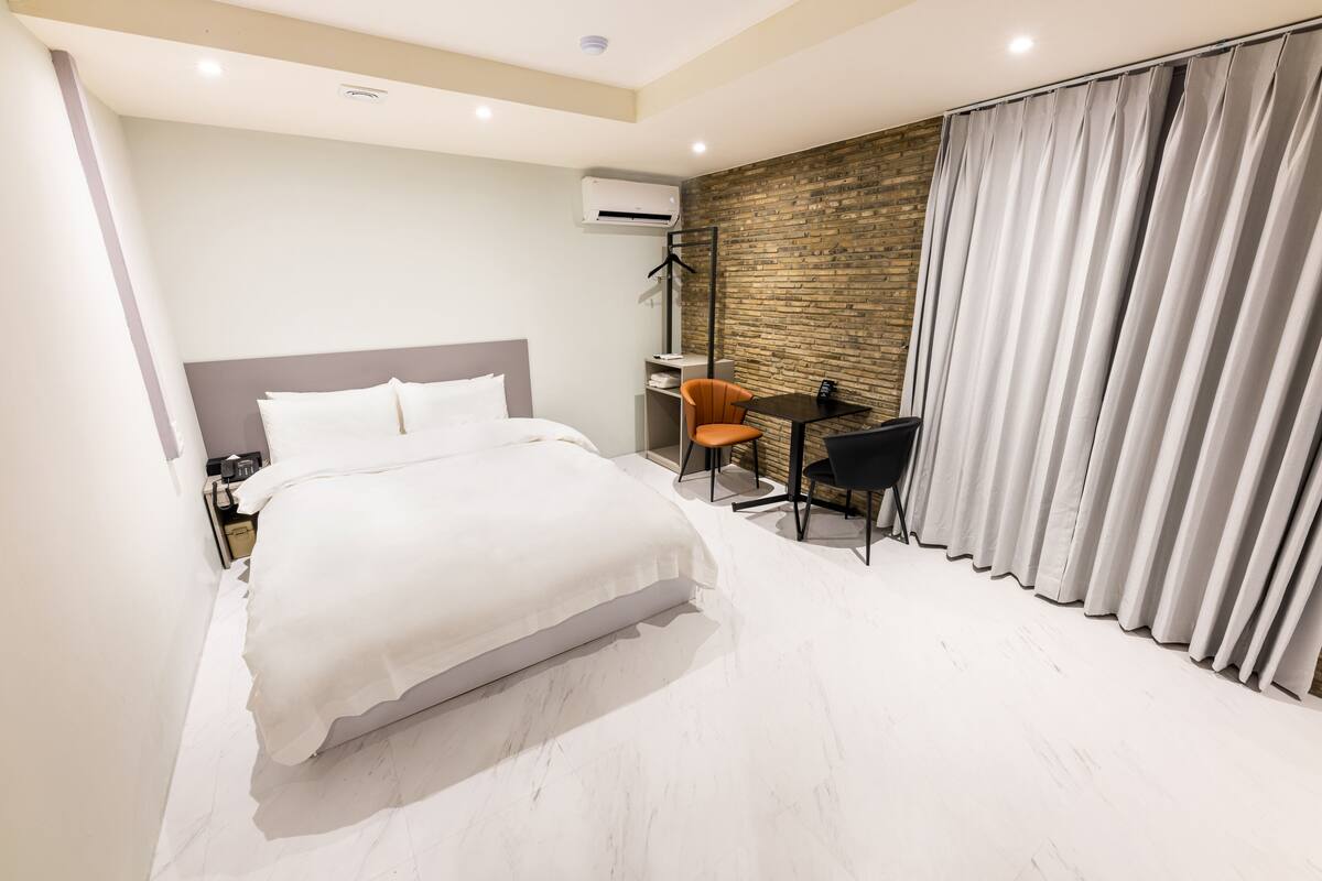 Une chambre d’hôtel moderne dotée d’un grand lit, d’un bureau avec une chaise et offrant une vue sur le paysage urbain par la fenêtre.
