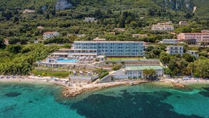 Un hotel frente al mar con piscina, playa y montañas al fondo.