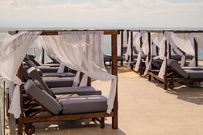A row of sun loungers with white canopies, arranged on a tiled deck with a view of the sea. - Alyssium (Corfu)
