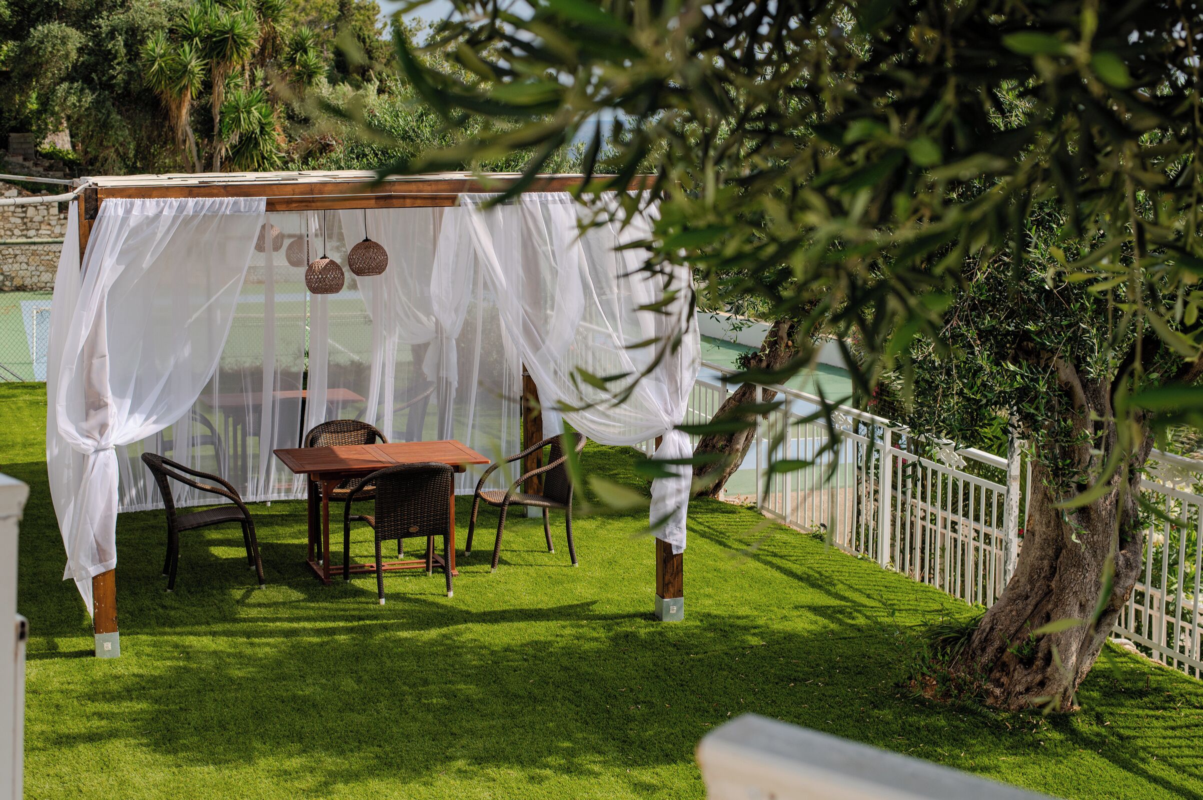 Un kiosque avec une table et des chaises, entouré d’une clôture blanche et de verdure.