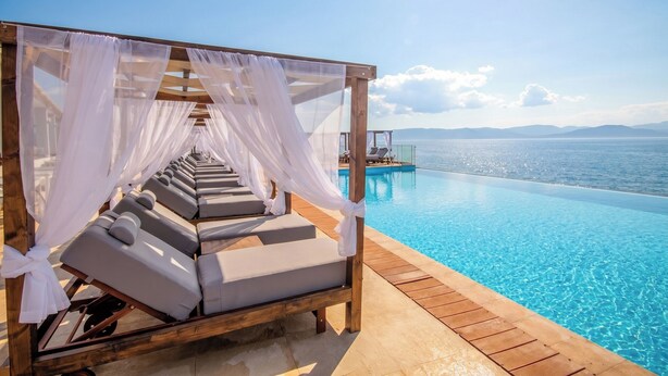 Un área de descanso junto a la piscina, con vistas al mar, una terraza de madera y un toldo de tela blanca.
