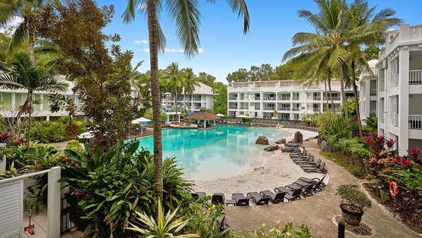 A resort with a central swimming pool, lounge chairs, and palm trees.