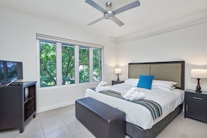 Relax in a spacious room with a large bed, flat-screen TV, and a window overlooking lush greenery.