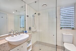 Enjoy a refreshing shower in the bathroom, featuring a sink, glass-enclosed shower and toilet with a window.