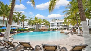 A resort pool with lounge chairs, palm trees, and a building labeled "The Beach Club". - Whispering Palms Beach Club Spa Suite (Palm Cove)