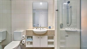A modern bathroom with a glass-enclosed shower, a white sink, and two toilets. - Whispering Palms Beach Club Spa Suite (Palm Cove)