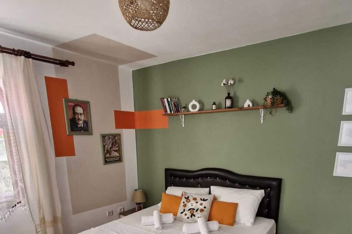 Une chambre à coucher avec un grand lit, une table de chevet, une commode, un luminaire suspendu et une étagère ornée d’objets décoratifs.