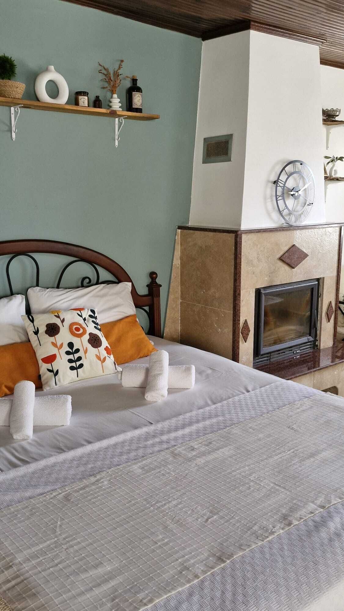 A bedroom with a bed, pillows, a clock, a fireplace, and shelves with decorative items.