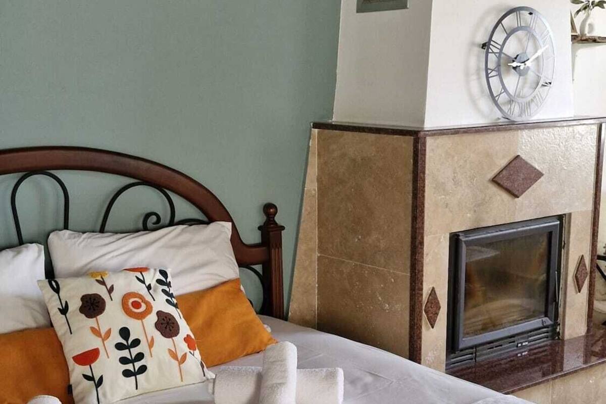 A bedroom with a bed, pillows, a clock, a fireplace, and shelves with decorative items.