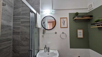 A bathroom with a glass shower enclosure, a sink with a mirror, and framed pictures on the wall.