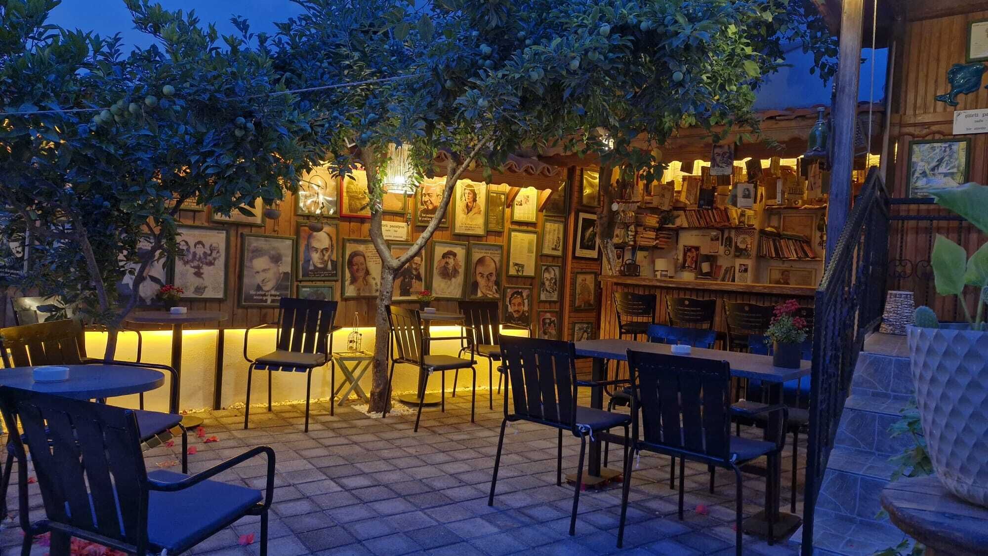 An outdoor seating area with tables and chairs, surrounded by walls adorned with framed pictures and books.