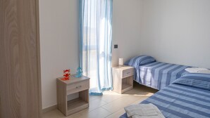 Ein Schlafzimmer mit zwei Betten, einem Nachttisch, einer Kommode und einem Fenster mit durchsichtigen Vorhängen.