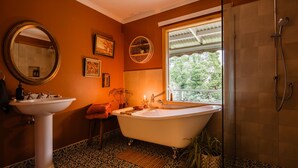 Een badkamer met een vrijstaand bad, een wastafel op voet, een grote spiegel en een douche met een glazen deur.