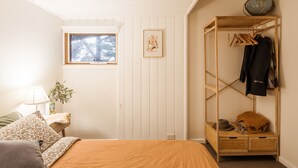 Een slaapkamer met een bed, een raam, een houten garderobe, een lamp en een ingelijst kunstwerk aan de muur.