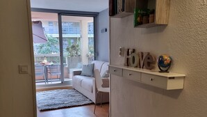 A modern living room with a sofa, a coffee table, and a small rug. There is a sliding glass door leading to an outdoor balcony with a table and chairs. - Studio in Residence with swimming pool and solarium, 5 minutes from the beach (Roquebrune-Cap-Martin)