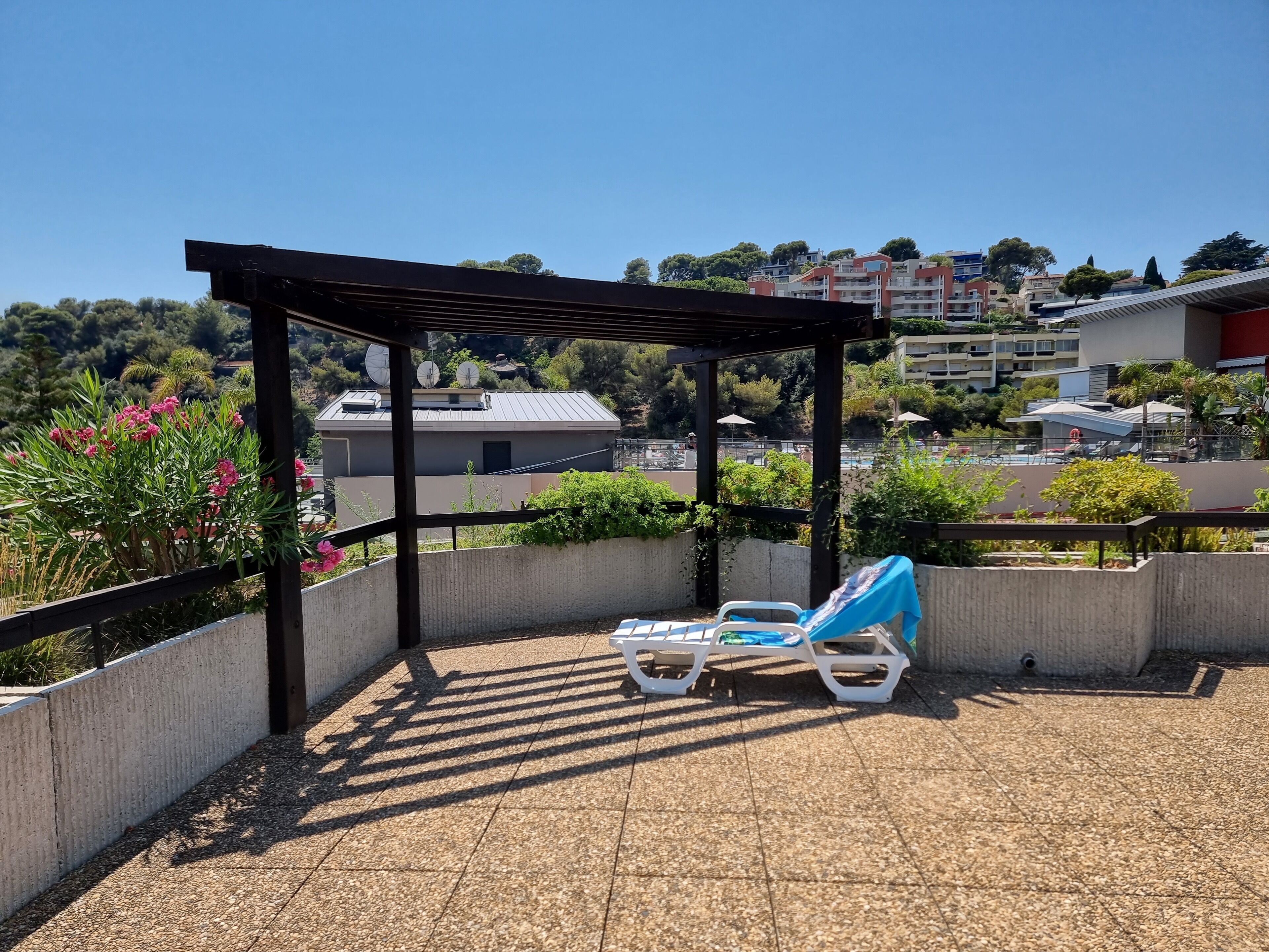 A rooftop terrace with two lounge chairs, a pergola, and a view of surrounding buildings.