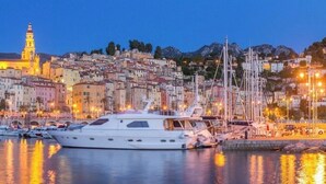 A marina with boats docked, a prominent church with a bell tower, and a densely packed hillside town with buildings. - Studio in Residence with swimming pool and solarium, 5 minutes from the beach (Roquebrune-Cap-Martin)