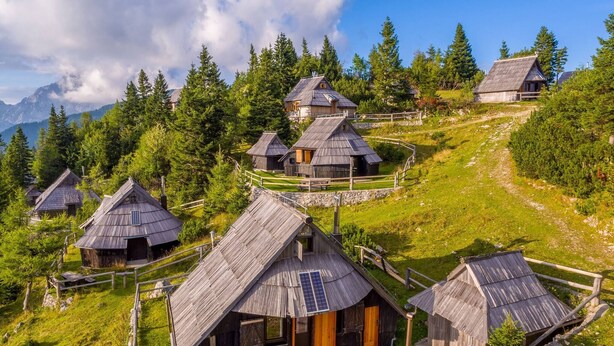 Eine Gruppe rustikaler Holzhütten mit Strohdächern, umgeben von üppiger Vegetation und Bergen im Hintergrund.