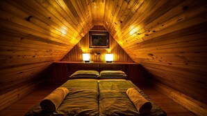 Ein gemütliches Schlafzimmer unter dem Dach mit Holzwänden, schrägen Decken, zwei Nachttischlampen und einem Bett mit grüner Bettwäsche und gerollten Handtüchern.