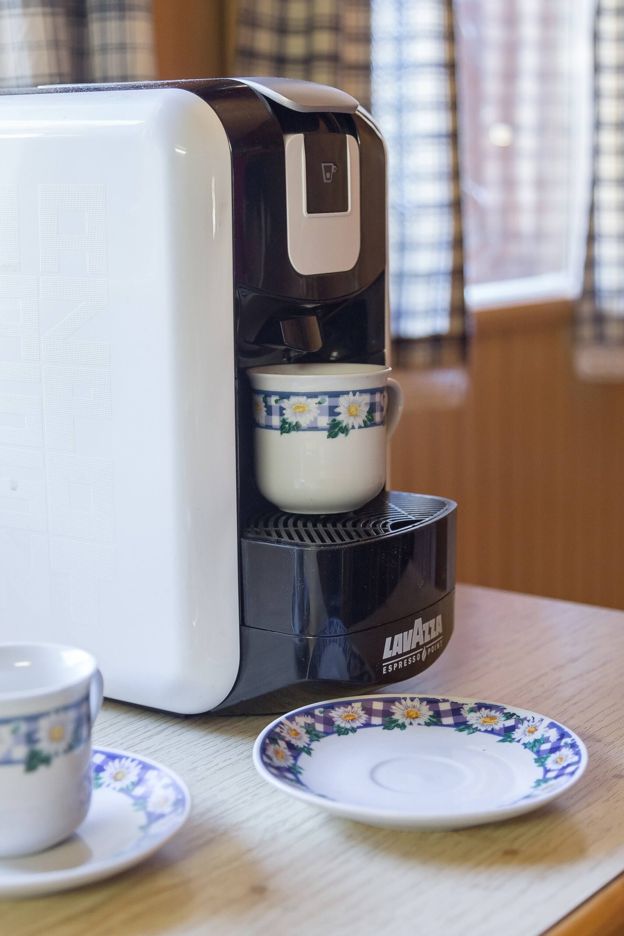 En kaffebryggare med en kopp och ett fat stående på ett träbord.