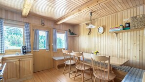 Ein Holzblockhaus-Interieur mit Esstisch, Stühlen, einer Bank, einer kleinen Küchenzeile und einem Fenster mit Vorhängen.