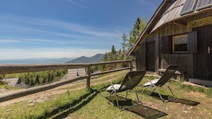 A rustic wooden building with solar panels, a wooden fence, and two metal chairs on a grassy area with a view of distant mountains. - Stunning Views - Chalet Encijan - Velika Planina (Kamnik)