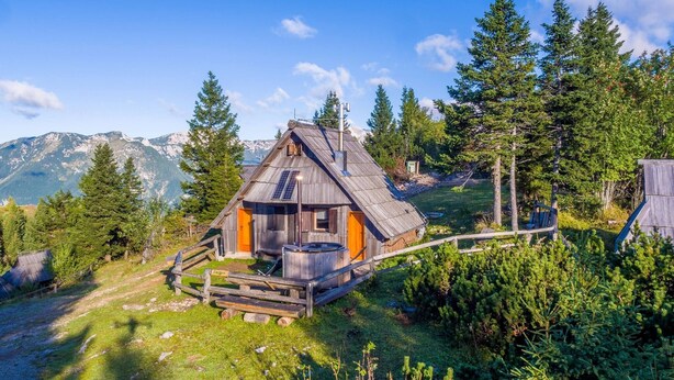 A rustic cabin with a sloped roof, surrounded by lush greenery and mountains in the background. - Stunning Views - Chalet Encijan - Velika Planina (Kamnik)