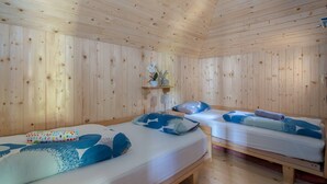 Ein Zimmer in einer Holzhütte mit zwei Betten, jeweils mit blau-weißer Bettwäsche, einem kleinen Regal mit einer Pflanze und einer Holzzieldecke.