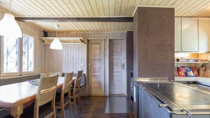A wooden dining area with a table and chairs, a kitchen with a stainless steel counter, and a door leading to another room. - Chalet Pehta - Velika Planina (Kamnik)