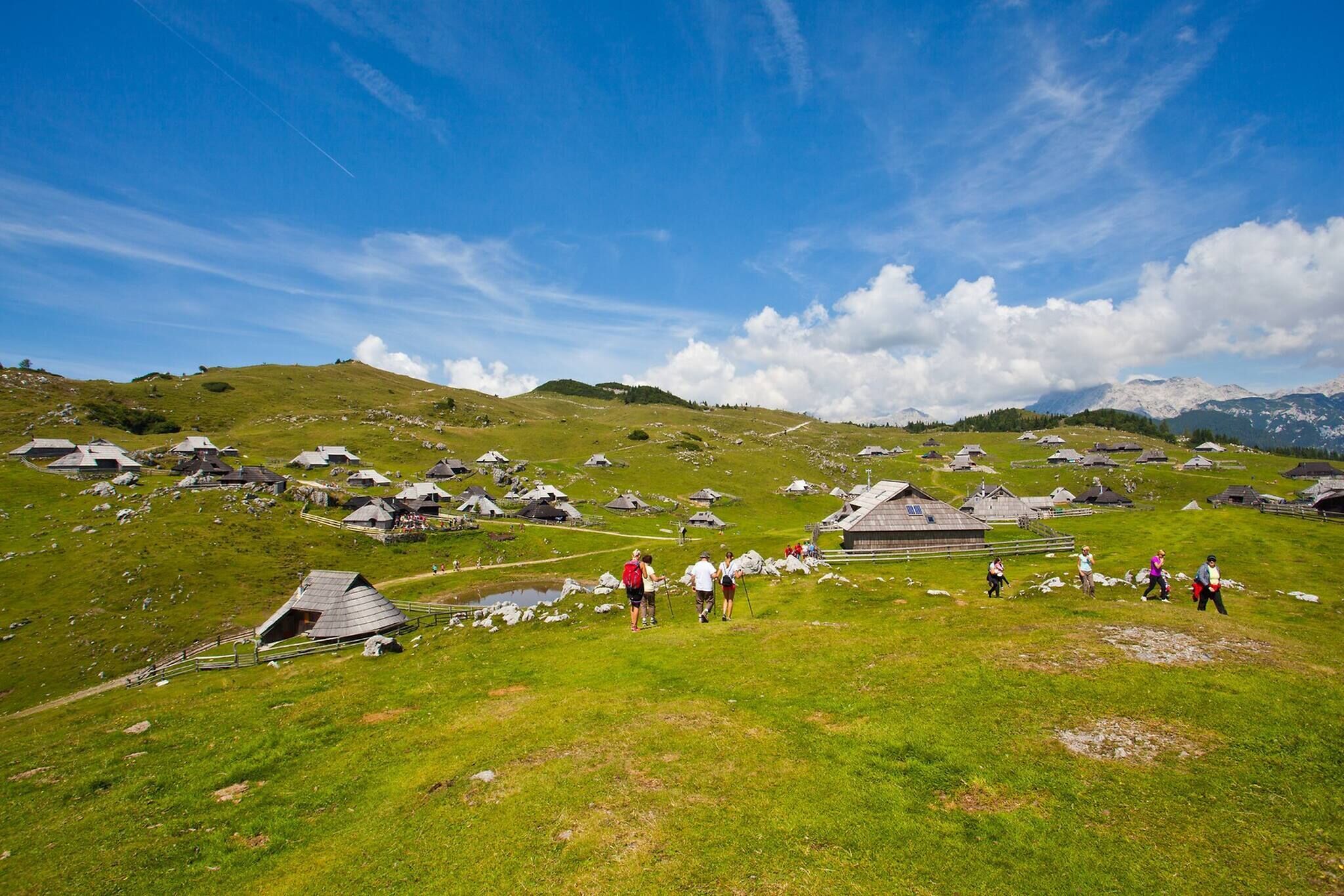 A rural landscape with multiple traditional houses on a hillside, a clear sky, and a few people walking.