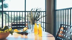 Een ronde tafel met een schaal fruit, een vaas met een plant en twee flessen sinaasappelsap.