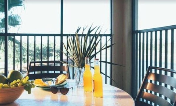 Uma mesa redonda com uma tigela de frutas, um vaso com uma planta e duas garrafas de suco de laranja.