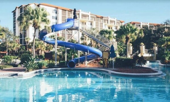 Ein Swimmingpool mit einer blauen Rutsche und einem mehrstöckigen Hotel im Hintergrund.