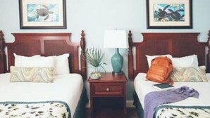 Een hotelkamer met twee bedden, elk met een houten hoofdbord, een nachtkastje met een lamp en ingelijste foto's aan de muur.