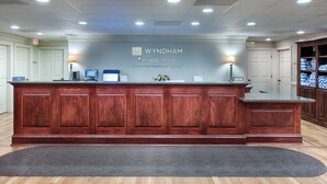 Un comptoir d’accueil avec un revêtement en bois, une enseigne indiquant « WYNDHAM Patriots’ Place » et un écran d’ordinateur.